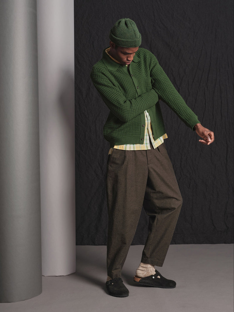Person wearing a green sweater and hat, standing against a dark wall.