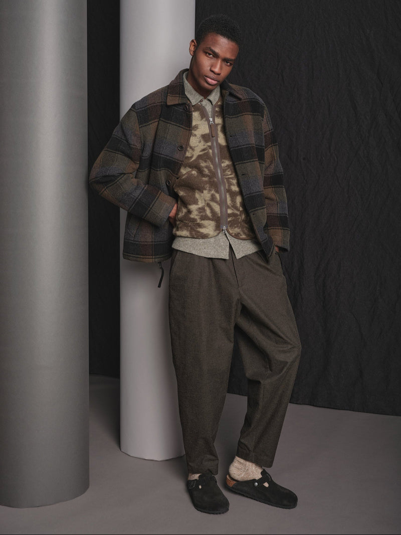 Man wearing a plaid jacket and camouflage shirt against a dark background