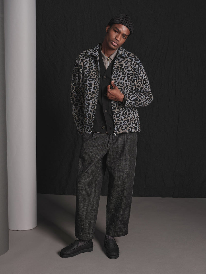 Man wearing a leopard print jacket and gray pants in a studio setting