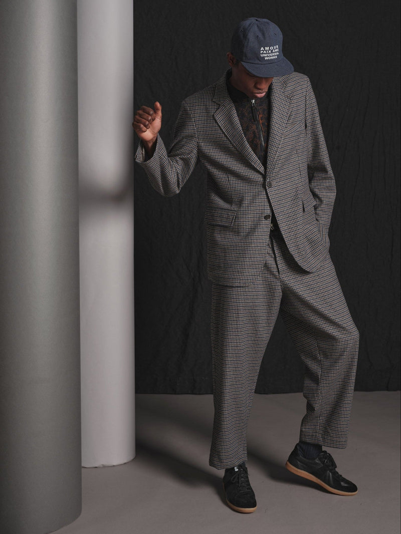 Person wearing a gray checkered suit and cap against a dark background
