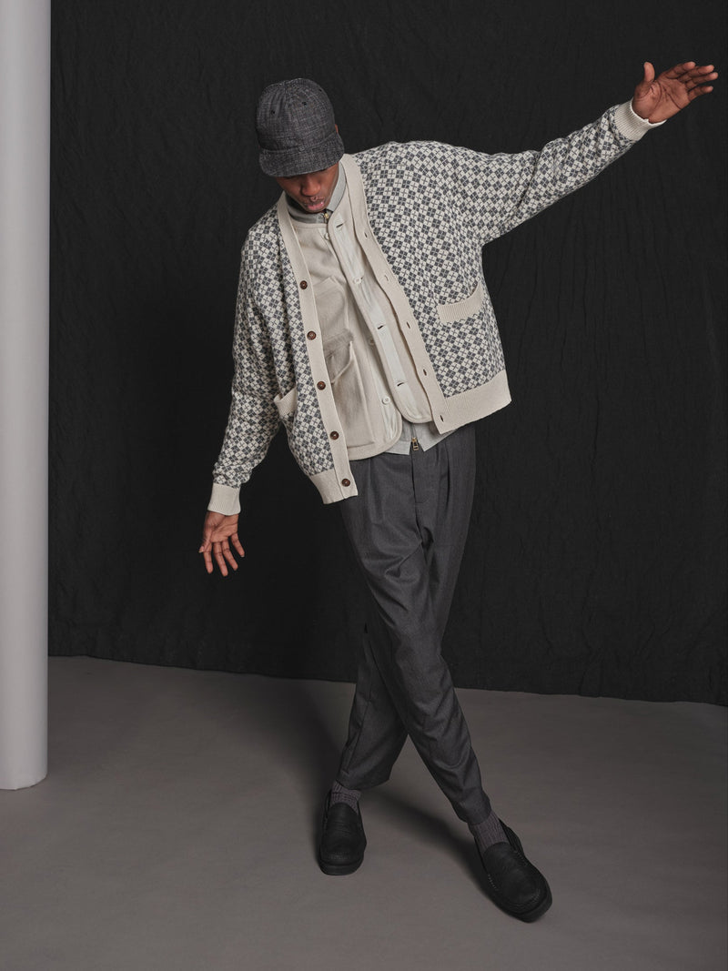 Person wearing a patterned jacket and cap against a black background