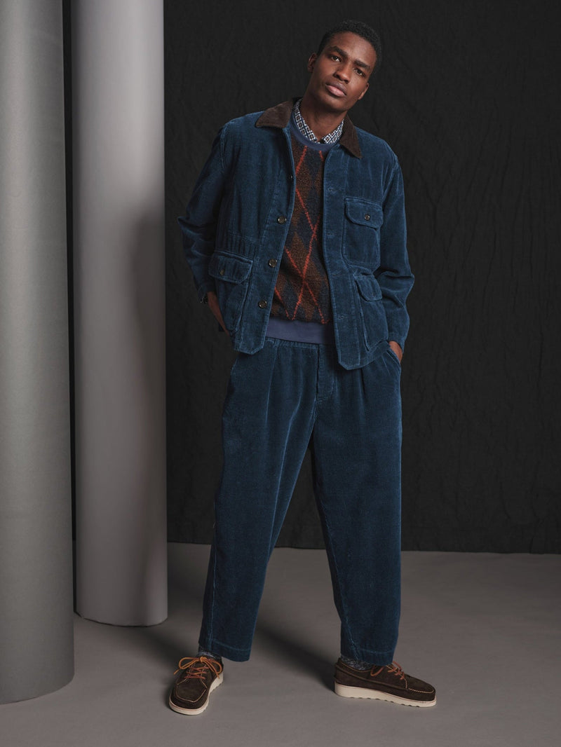 Man wearing a blue corduroy outfit standing against a dark background