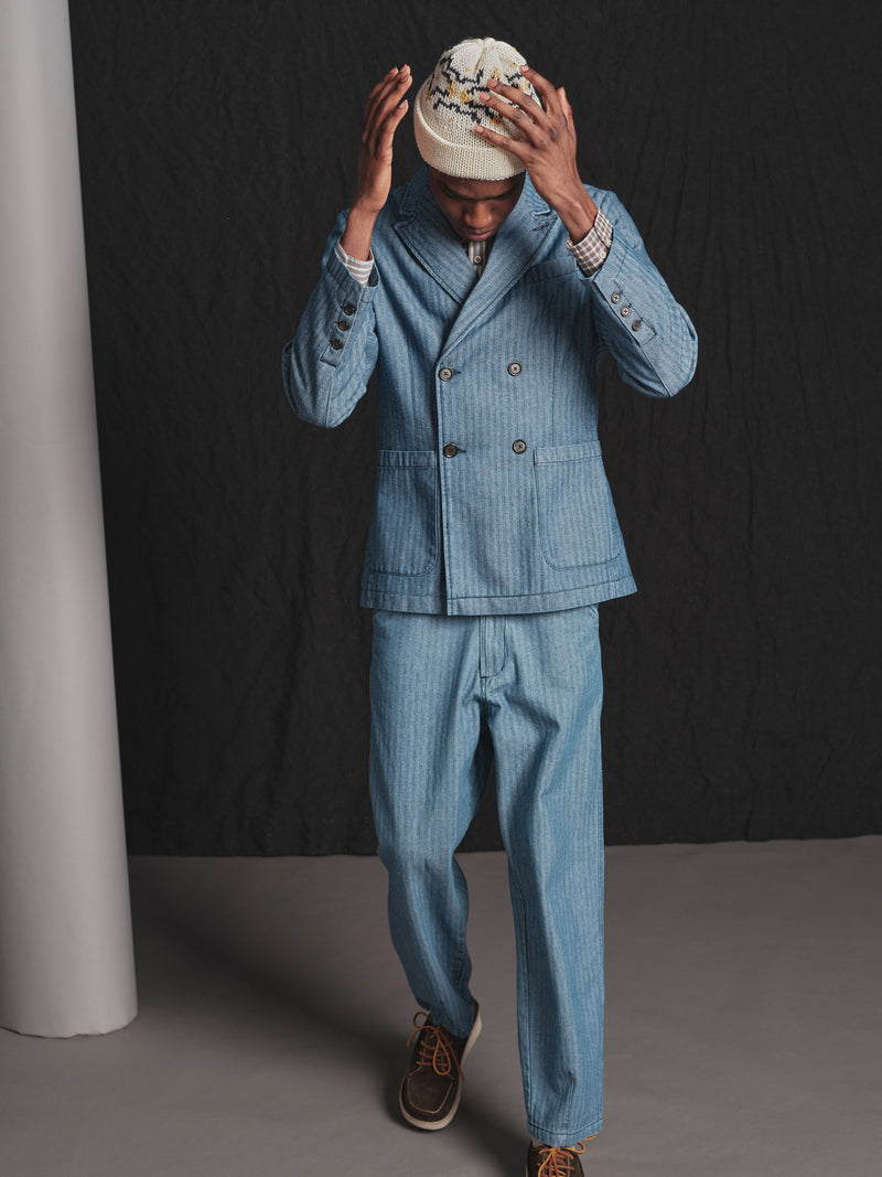 Person wearing a blue denim suit and white cap against a black background