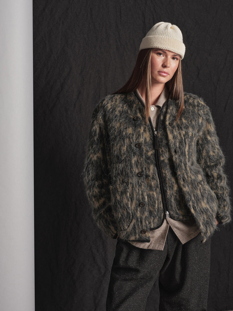 Person wearing a fuzzy fabric cardigan and beige beanie against a dark background