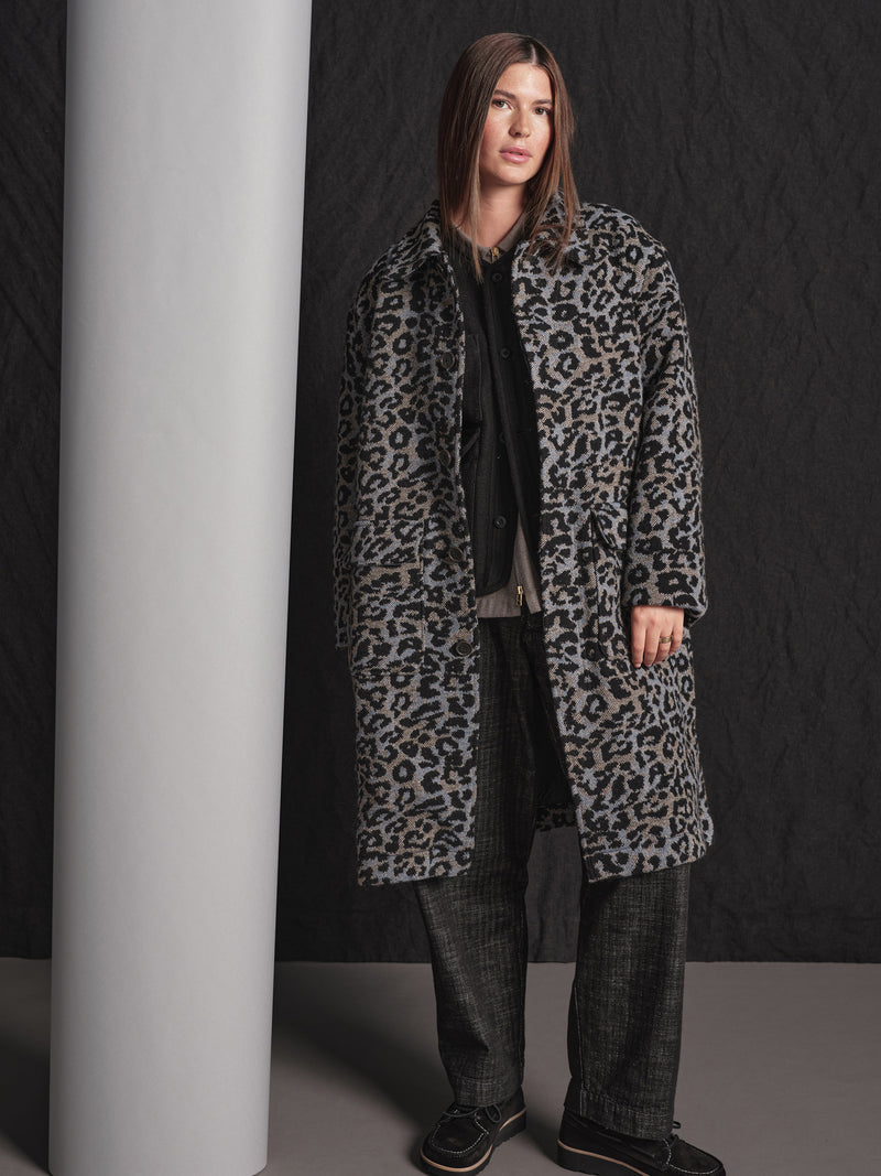 Person wearing a leopard print coat against a black background