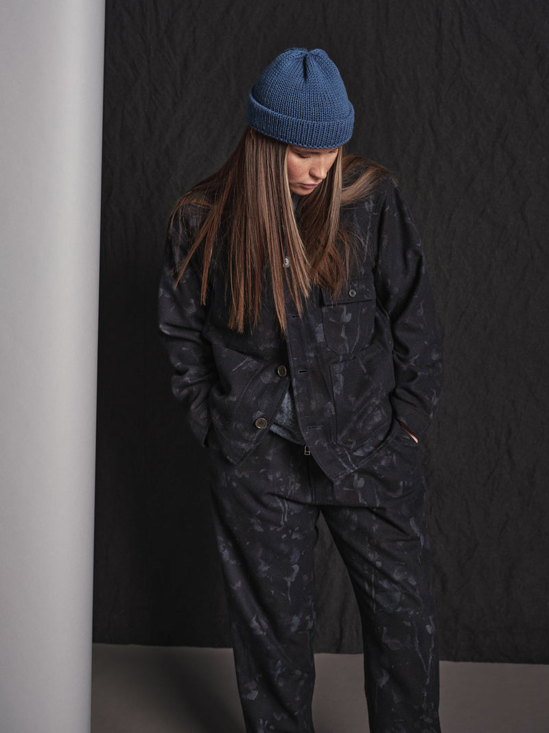 Person wearing a blue beanie and dark camouflage outfit against a black background