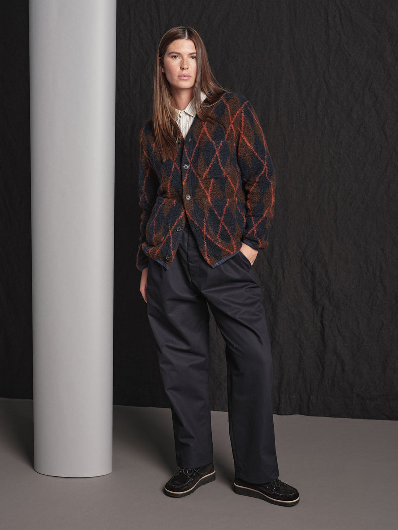 Person wearing an argyll cardigan and dark pants against a black background
