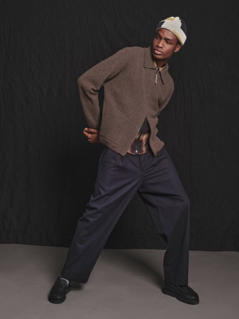 Person wearing a brown sweater and dark pants against a black background